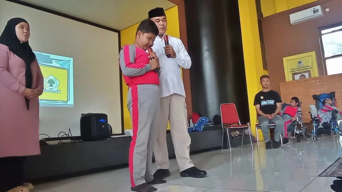 Seorang siswa SLB Negeri Cinta Asih Soreang (berdiri di tengah) di Kabupaten Bandung, Jawa Barat dan Ketua DPD Golkar Kabupaten Bandung, Sugianto saat melantunkan doa salat dhuha bersama siswa lainnya di Aula DPD Golkar Kabupaten Bandung, Kamis (11/12/2025). Foto: cep/trustjabar